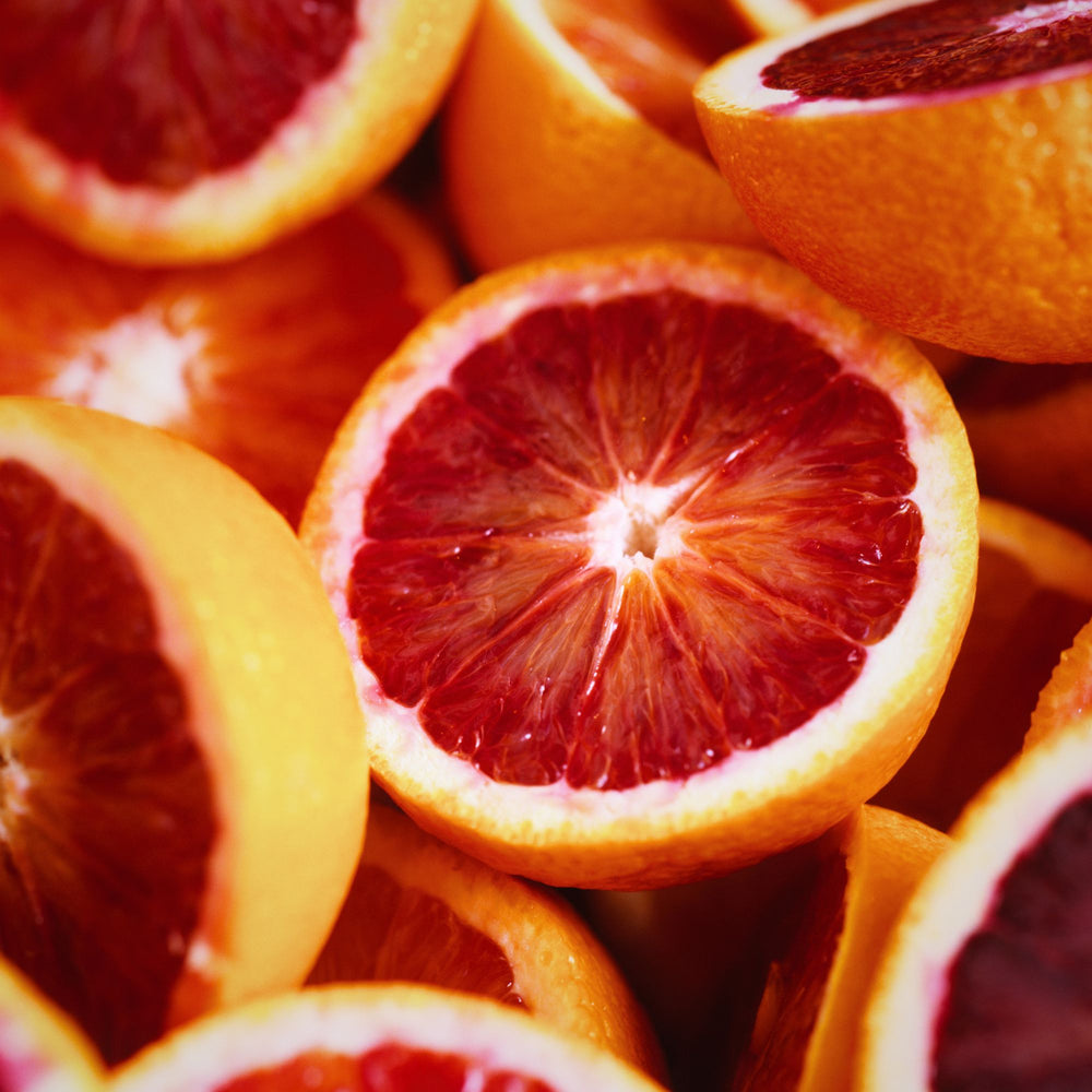 A sea of halved blood oranges piled on top of one another, their deep red flesh revealed.