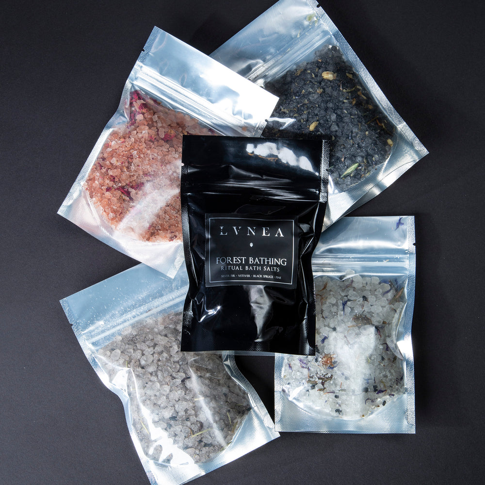 4 ounce black resealable pouches of all 5 of LVNEA's ritual bath salts. Includes: Fire Bathing, River Bathing, Ocean Bathing, Forest Bathing, and Lunar Bathing lying flat on a black background