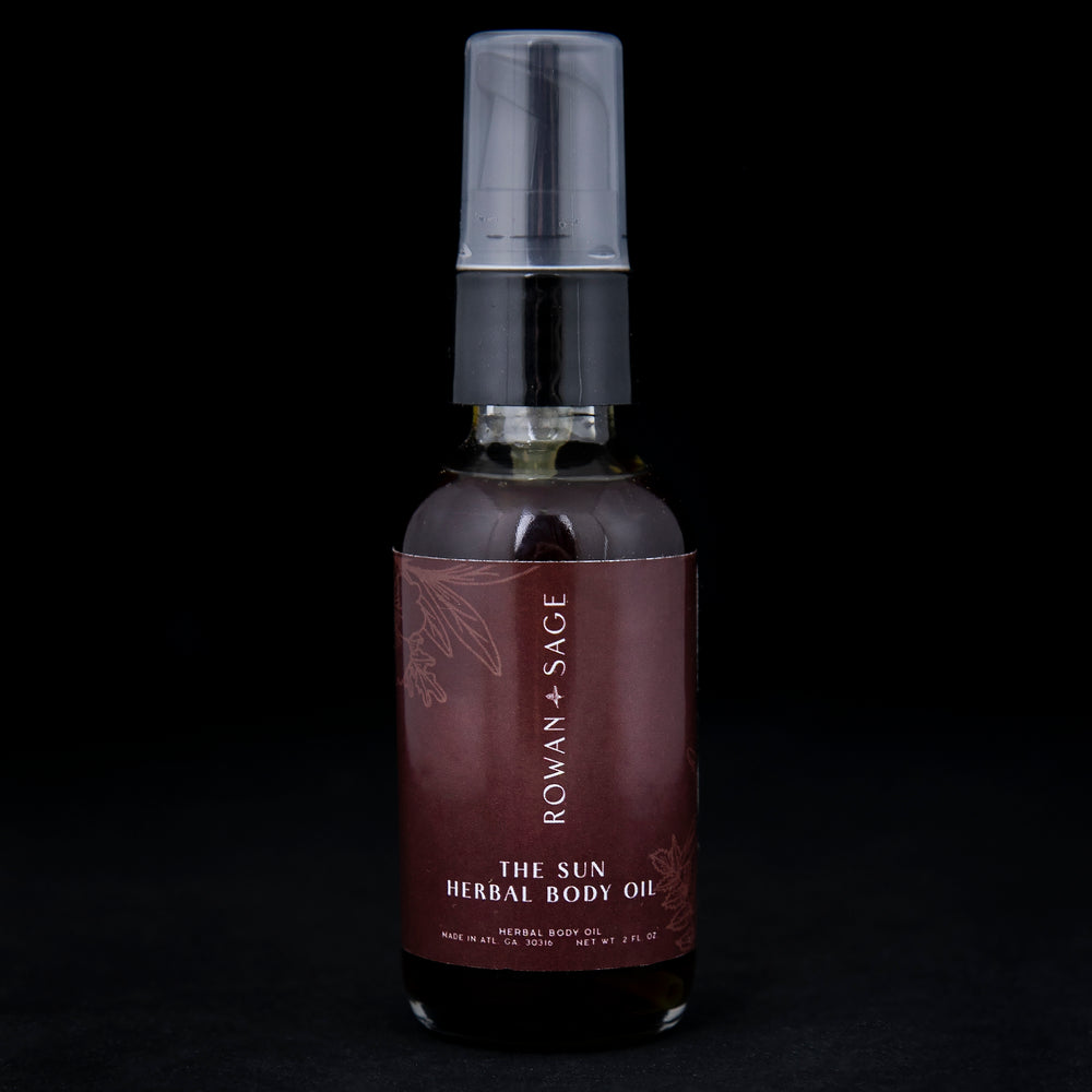 2oz glass bottle with pump top and burgundy label, containing Rowan + Sage's "The Sun" body oil on black background.