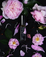 8ml glass bottle of Babylon Rose, glistening with dew drops, surrounded by fresh roses and seen from overhead.