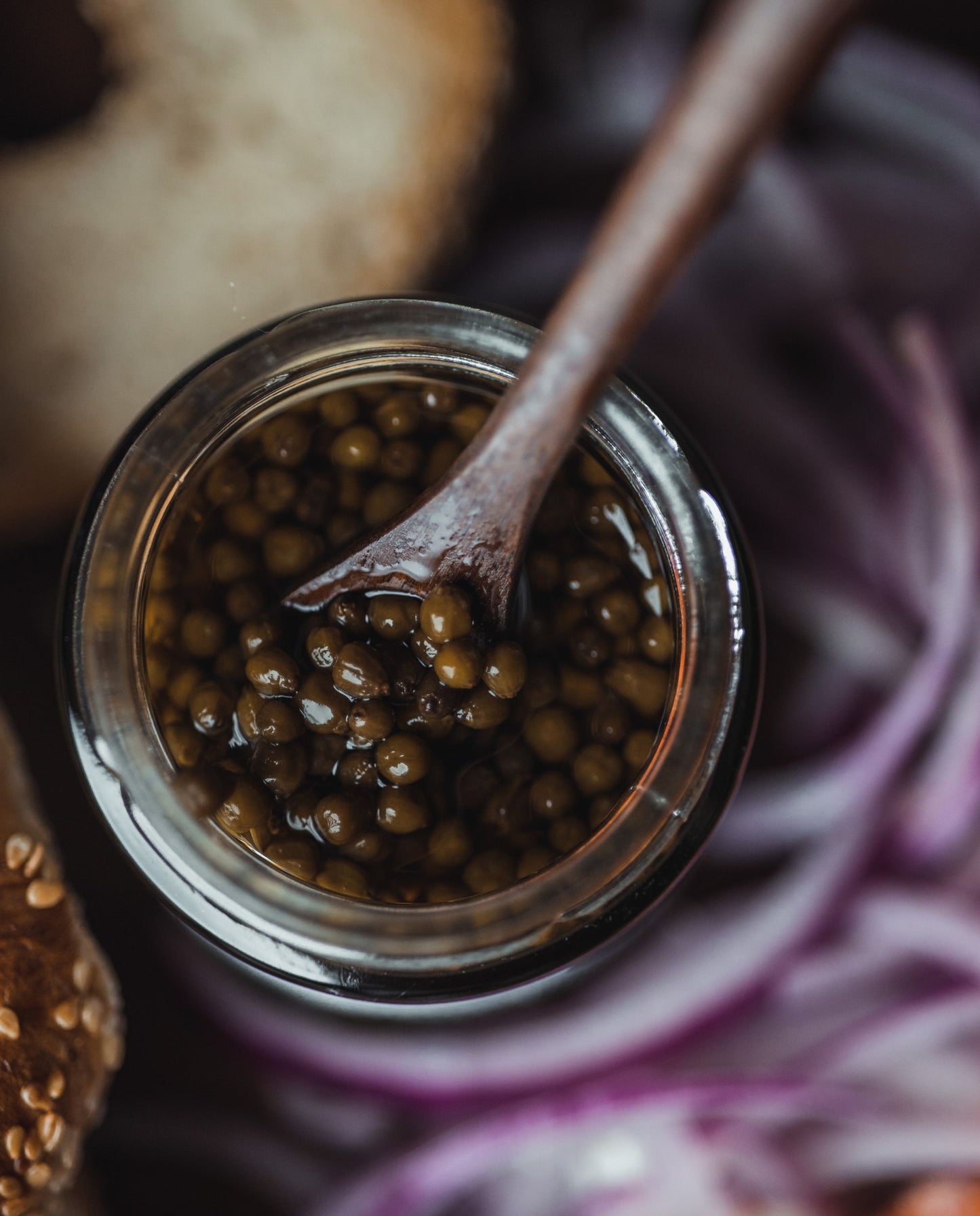 close up of open jar of elderberry capers with a wooden spoon in it