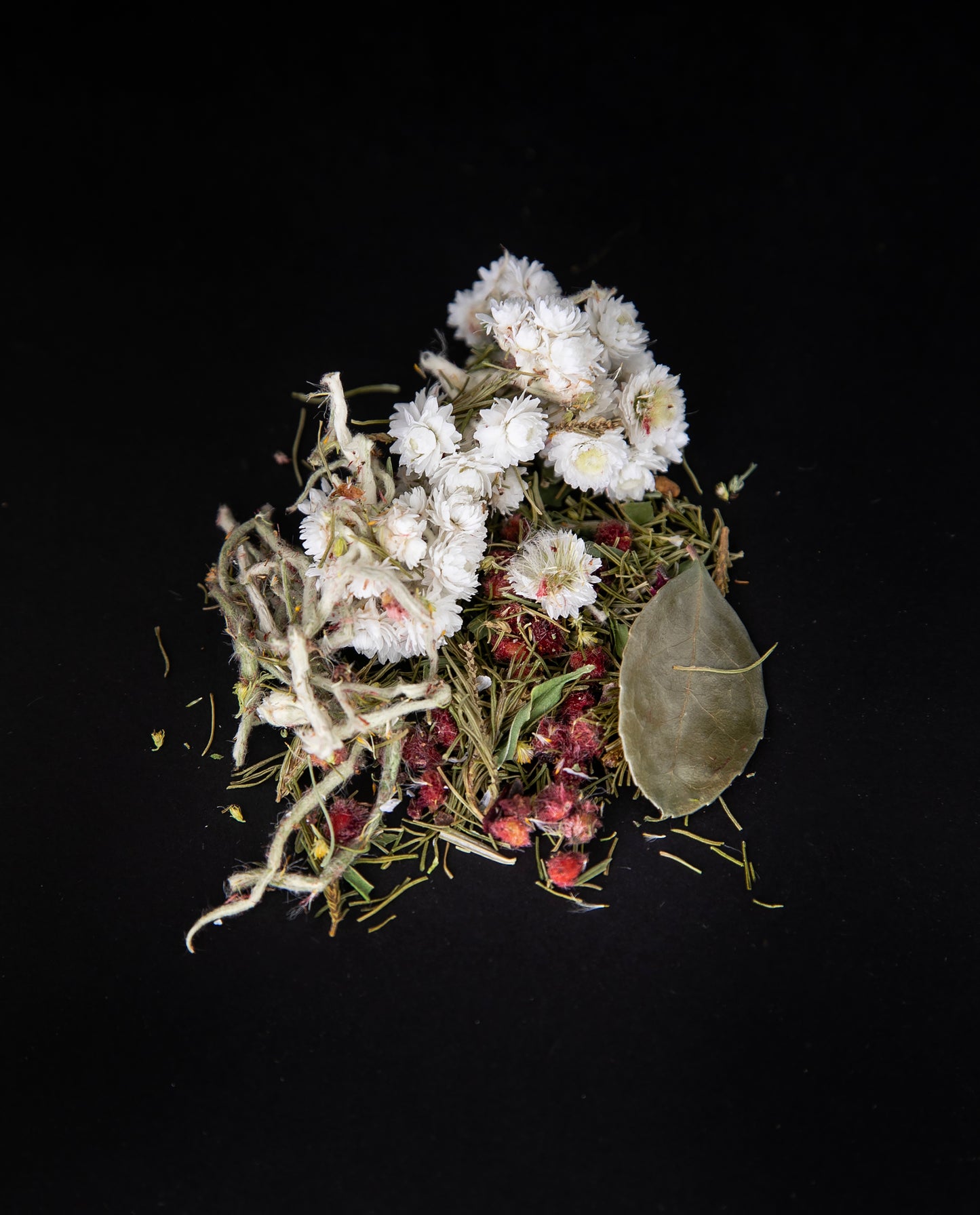 Handful of loose leaf "Été nordique" tea on a black background. The blend features sumac berries and whole imortelle flowers.