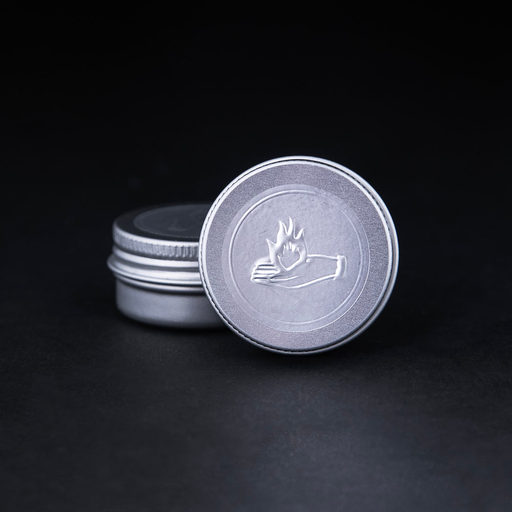 
                      
                        2g sample of LVNEA's "Fire and Oud" solid perfume presented in a metal tin. The lid is embossed with an illustration of a hand holding a flame.
                      
                    