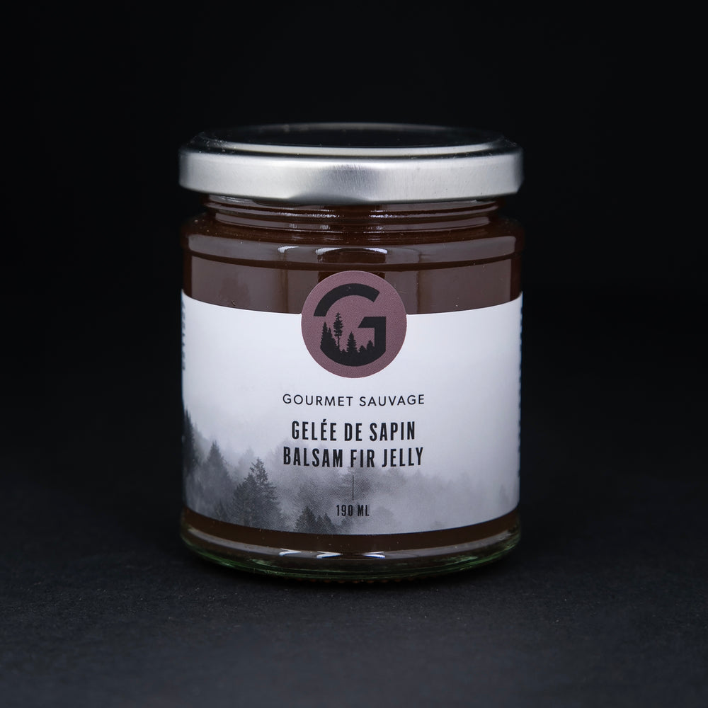 Clear glass jar with metal lid of Gourmet Sauvage's balsam fir jelly, sitting on black background