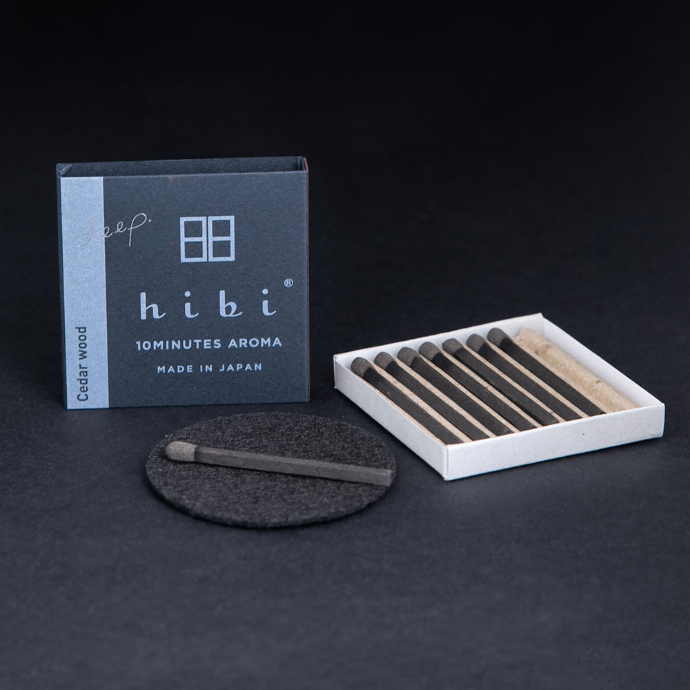 
                      
                        open box of HIBI incense matches, individual matches are nestled in a corrugated cardboard insert, a match is sitting on a small heatproof  burn mat
                      
                    