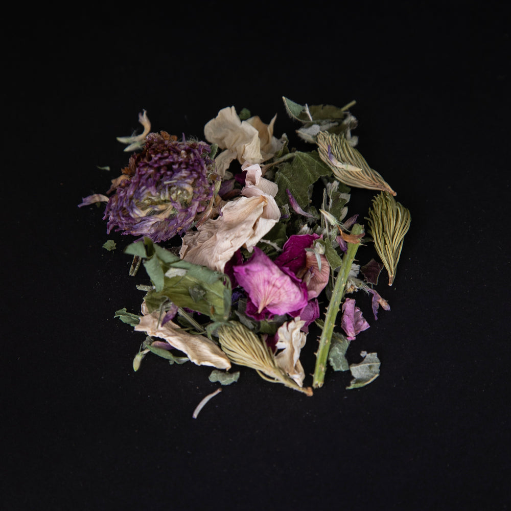 handful of loose "La Florale" tea on a black background. The herbal blend is colourful and includes rose petals, spruce tips, and and clover buds.