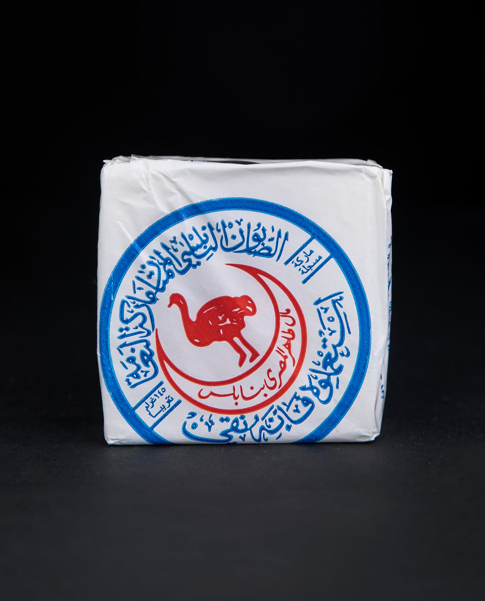 Bar of Palestinian olive oil soap wrapped in white wax paper, stamped with a blue and red ostrich seal