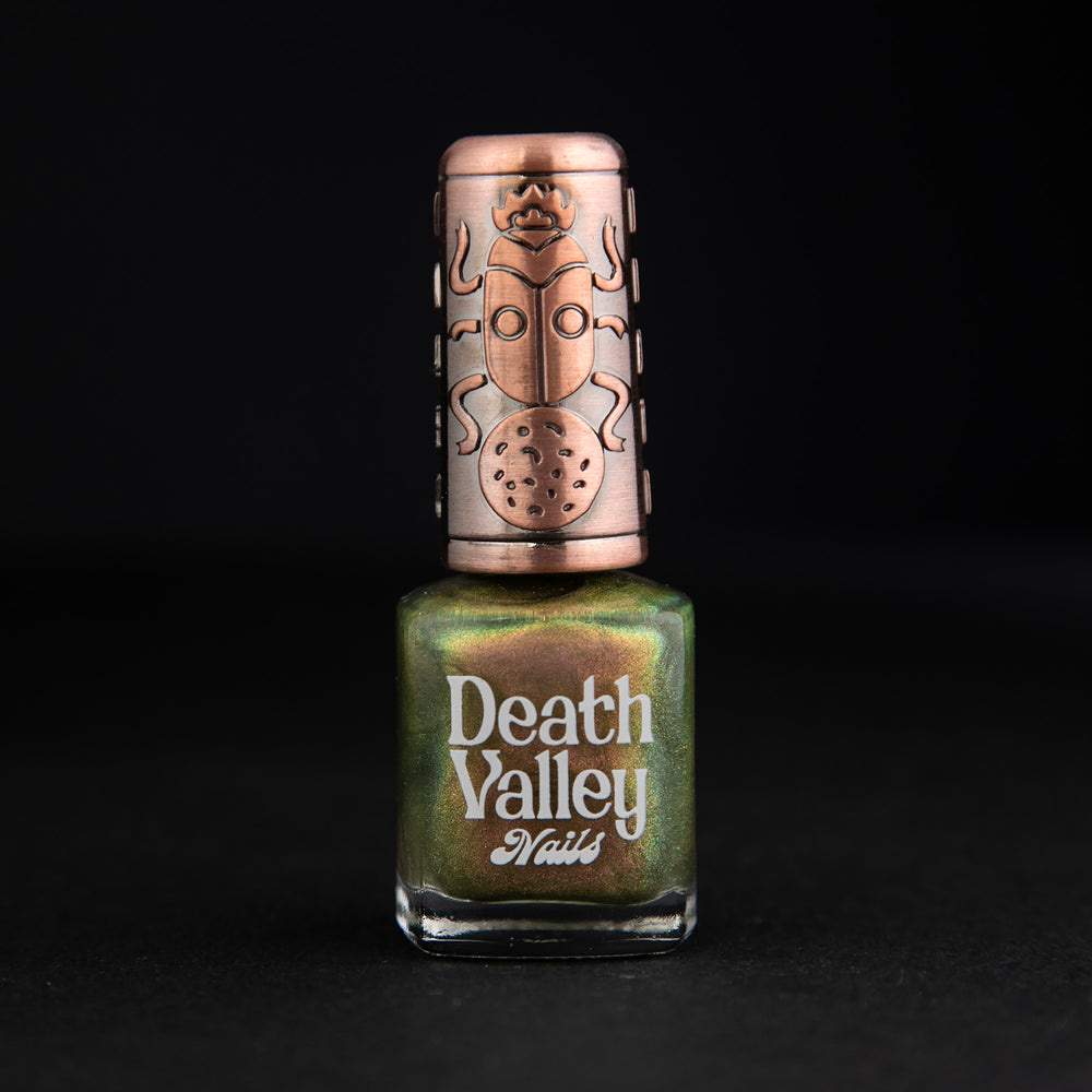 Bottle of "Eating Heads" nail polish on black background. The polish has a green base with multichrome shimmery finish.