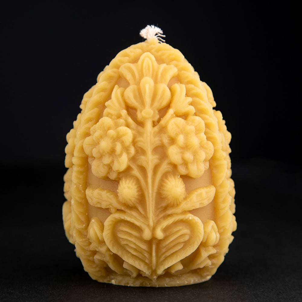 Carved egg-shaped beeswax candle with intricate floral designs on black background