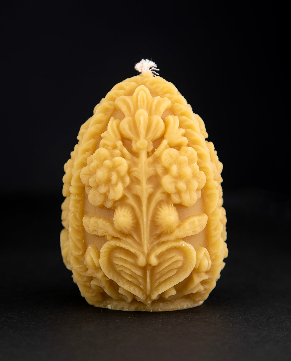 Carved egg-shaped beeswax candle with intricate floral designs on black background