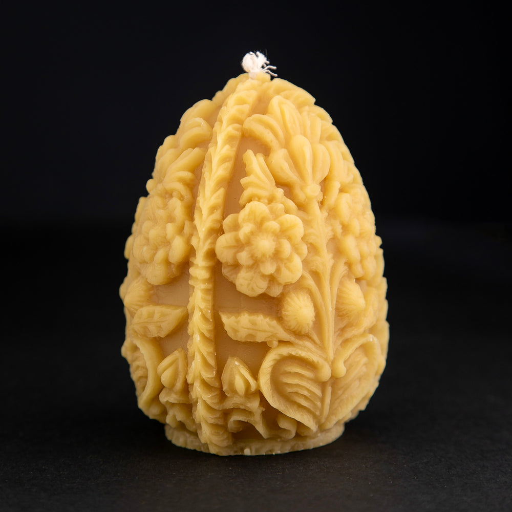 Carved egg-shaped beeswax candle with intricate floral designs on black background