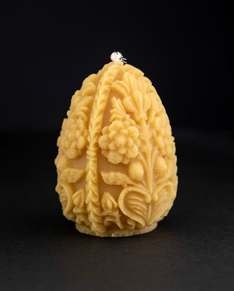 Carved egg-shaped beeswax candle with intricate floral designs on black background