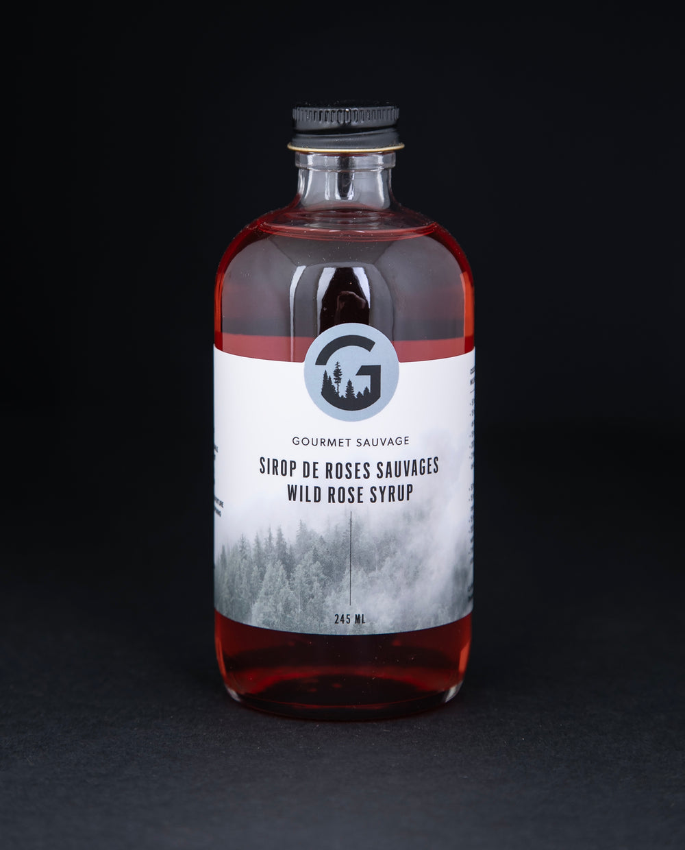 Clear bottle of Gourmet Sauvage's wild rose syrup, sitting on black background