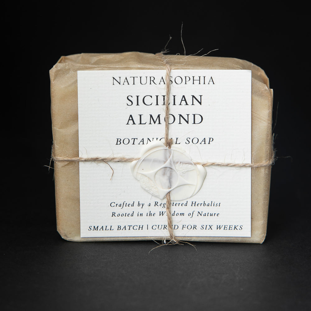 
                      
                        Bar of Naturasophia soap wrapped in brown paper and twine, with a label that reads "Sicilian Almond". There is a white wax stamp holding the label in place.
                      
                    