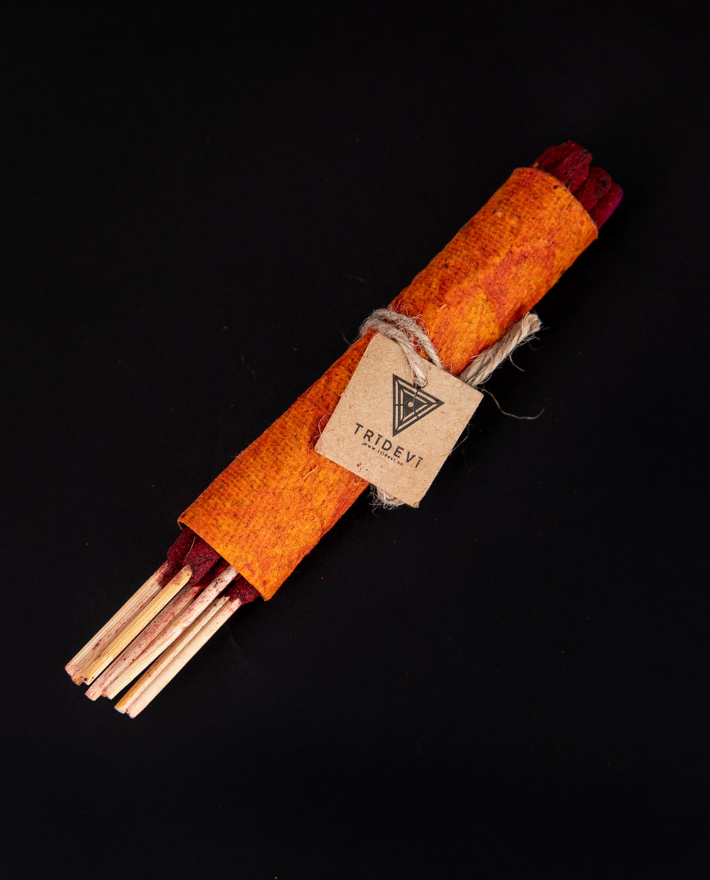 bundle of TriDevi 'Red Lotus' incense sticks wrapped in handmade orange paper, against a black background