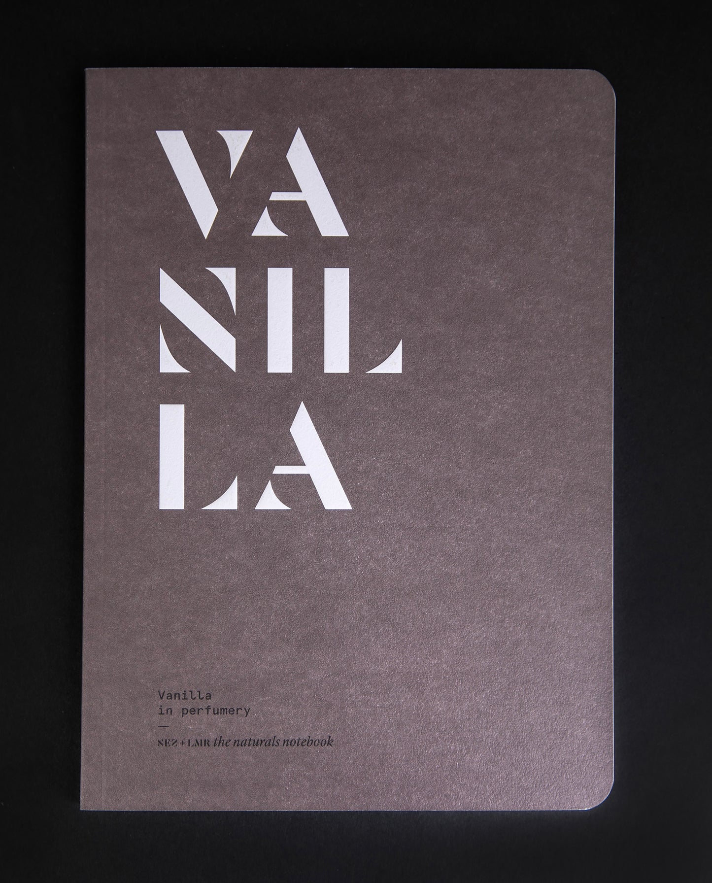 "Vanilla in Perfumery" book against black background. The cover is brown and features the word "VANILLA" in bold, graphic, white lettering.